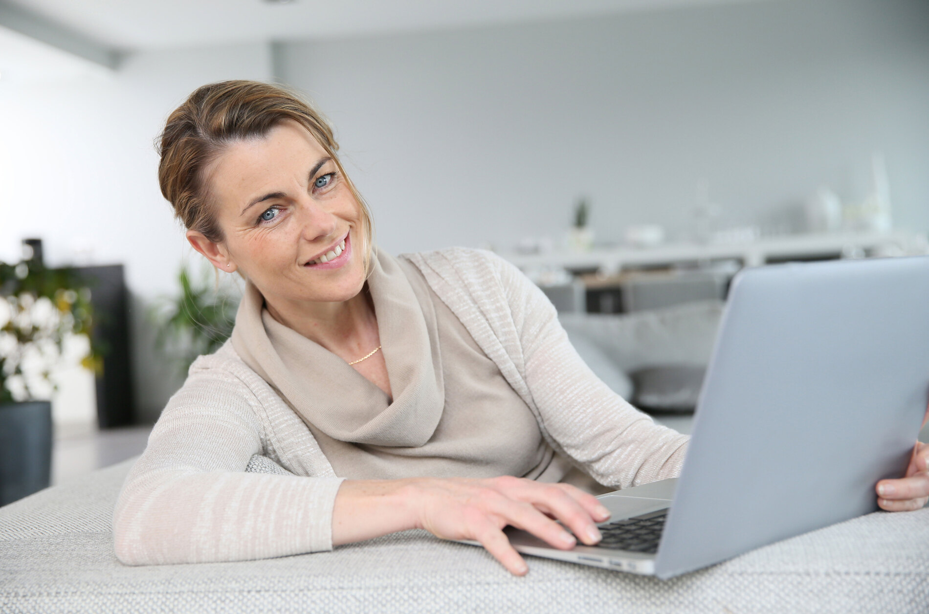 Reife Frau, die am Sofa sitzt und mit einem Laptop im Internet surft